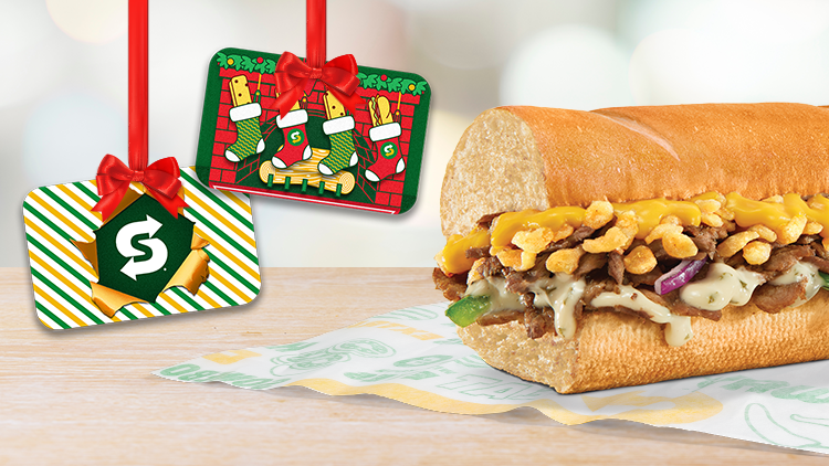 Sub de seis pulgadas de bistec con queso y ajo con dos tarjetas de regalo navideñas de Subway colgando del marco.